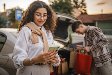 boyfriend pack shopping bags into trunk while girlfriend use cellphone