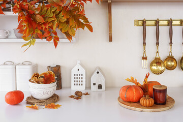 Fall decor with orange pumpkins, autumn leaves in cozy setting on white kitchen background