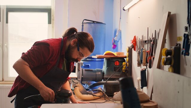 African american carpenter in joinery watching apprentice using orbital sander on lumber. Team in woodworking shop using angle grinder to create wooden decorations, refining wood objects, camera B