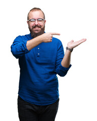 Fototapeta premium Young caucasian hipster man wearing glasses over isolated background amazed and smiling to the camera while presenting with hand and pointing with finger.