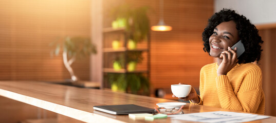 Smiling young black businesswoman drinking coffe at cafe, having conversation by phone, copy space