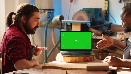 Upbeat men using CAD software on isolated screen laptop, debating wood design to use. Smiling cabinetmakers chatting, using program on chroma key notebook to make furniture schematics, camera A