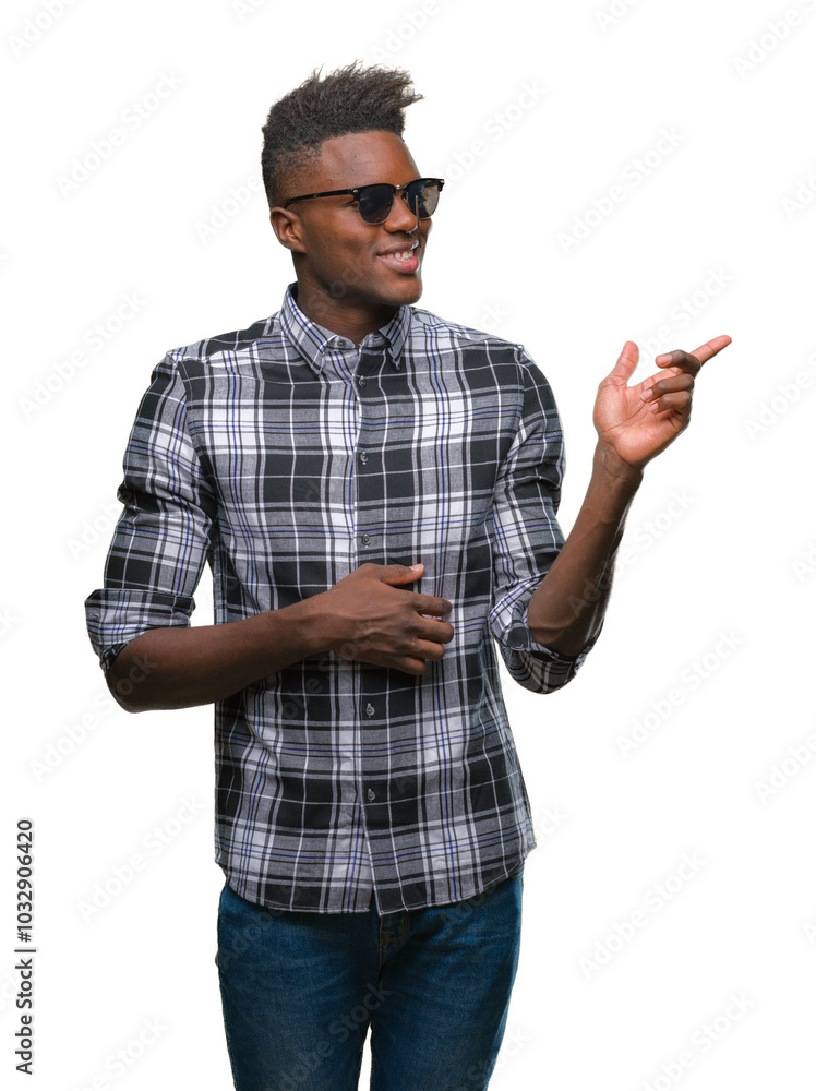 Wall mural Young african american man wearing sunglasses over isolated background with a big smile on face, pointing with hand and finger to the side looking at the camera.