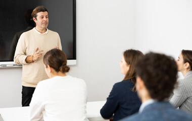 Fototapeta premium Middle-aged male teacher near interactive board explaining rules to group of students in classroom. Concept of studying of foreign language
