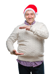 Handsome senior man wearing christmas hat over isolated background gesturing with hands showing big and large size sign, measure symbol. Smiling looking at the camera. Measuring concept.