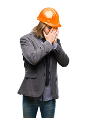 Young handsome architec man with long hair wearing safety helmet over isolated background with sad expression covering face with hands while crying. Depression concept.