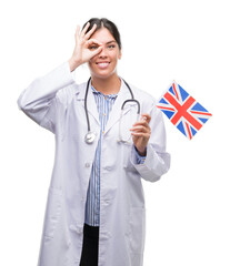 Young hispanic doctor woman holding flag of united kingdom with happy face smiling doing ok sign with hand on eye looking through fingers