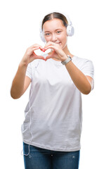 Young caucasian woman listening to music wearing headphones over isolated background smiling in love showing heart symbol and shape with hands. Romantic concept.