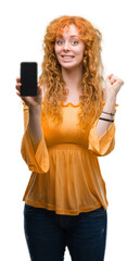 Young redhead woman showing smartphone screaming proud and celebrating victory and success very excited, cheering emotion