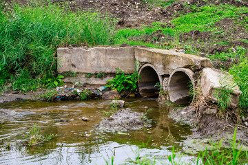 A dirty, muddy ditch with two pipes coming out of it