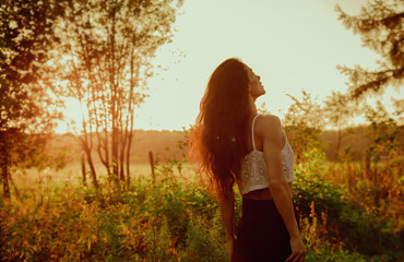Beautiful enjoying happy woman looking up with long brown hair style on sunset red orange summer...