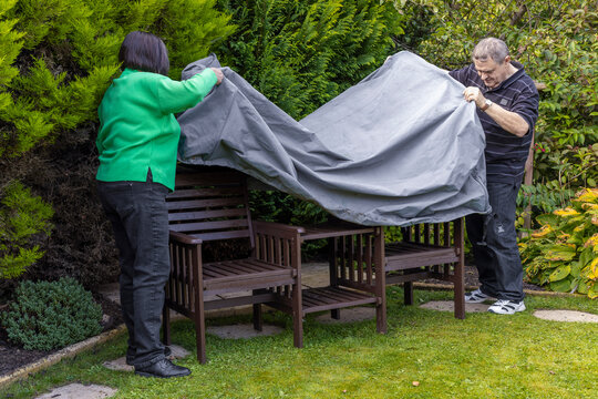 Senior couple put garden seat cover onto outdoor furniture bench set in home backyard garden ready for winter