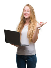 Naklejka premium Blonde teenager woman using computer laptop very happy pointing with hand and finger to the side