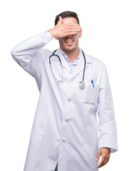 Fototapeta premium Handsome young doctor man smiling and laughing with hand on face covering eyes for surprise. Blind concept.
