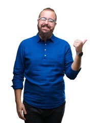 Young caucasian hipster man wearing glasses over isolated background smiling with happy face looking and pointing to the side with thumb up.