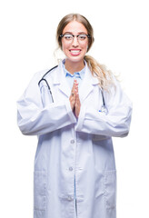 Beautiful young blonde doctor woman wearing medical uniform over isolated background praying with hands together asking for forgiveness smiling confident.