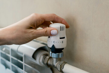 A woman's hand regulates the temperature of the central heating in the apartment.