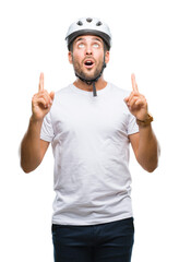 Young handsome man wearing cyclist safety helmet over isolated background amazed and surprised looking up and pointing with fingers and raised arms.