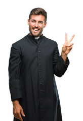 Young catholic christian priest man over isolated background smiling with happy face winking at the camera doing victory sign. Number two.
