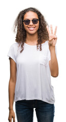 Young hispanic woman wearing sunglasses showing and pointing up with fingers number three while smiling confident and happy.