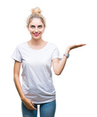 Young beautiful blonde woman wearing white t-shirt over isolated background smiling cheerful presenting and pointing with palm of hand looking at the camera.