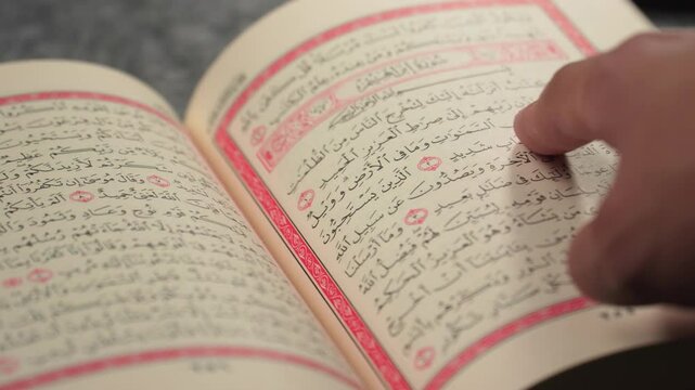 Quran (Koran) - close up of holy book of Muslims, with a man's hand pointing and reading it