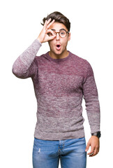 Young handsome man wearing glasses over isolated background doing ok gesture shocked with surprised face, eye looking through fingers. Unbelieving expression.