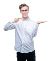 Young handsome blond man amazed and smiling to the camera while presenting with hand and pointing with finger.