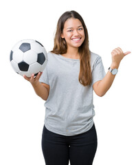 Young beautiful brunette woman holding soccer football ball over isolated background pointing and showing with thumb up to the side with happy face smiling