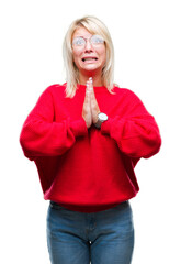 Young beautiful blonde woman wearing sweater and glasses over isolated background begging and praying with hands together with hope expression on face very emotional and worried.