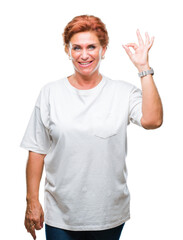 Atrractive senior caucasian redhead woman over isolated background smiling positive doing ok sign with hand and fingers. Successful expression.