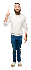 Young hipster man wearing winter sweater showing and pointing up with finger number one while smiling confident and happy.