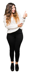 Young beautiful woman wearing white sweater Looking proud, smiling doing thumbs up gesture to the side