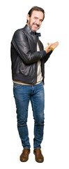 Middle age handsome man wearing black leather jacket Inviting to enter smiling natural with open hand