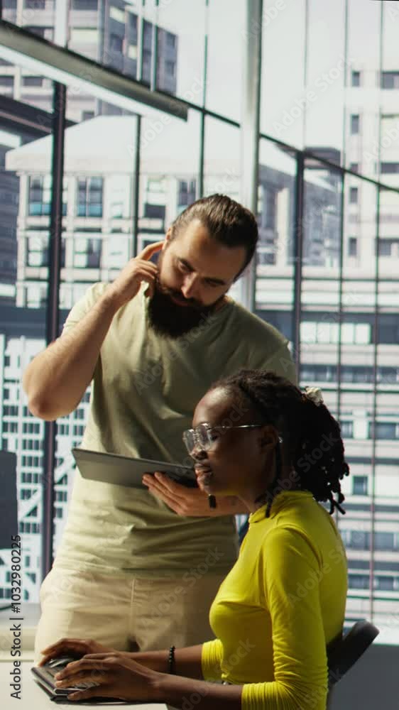 Poster vertical video manager coming to check on it employee at office desk testing and deploying programs 