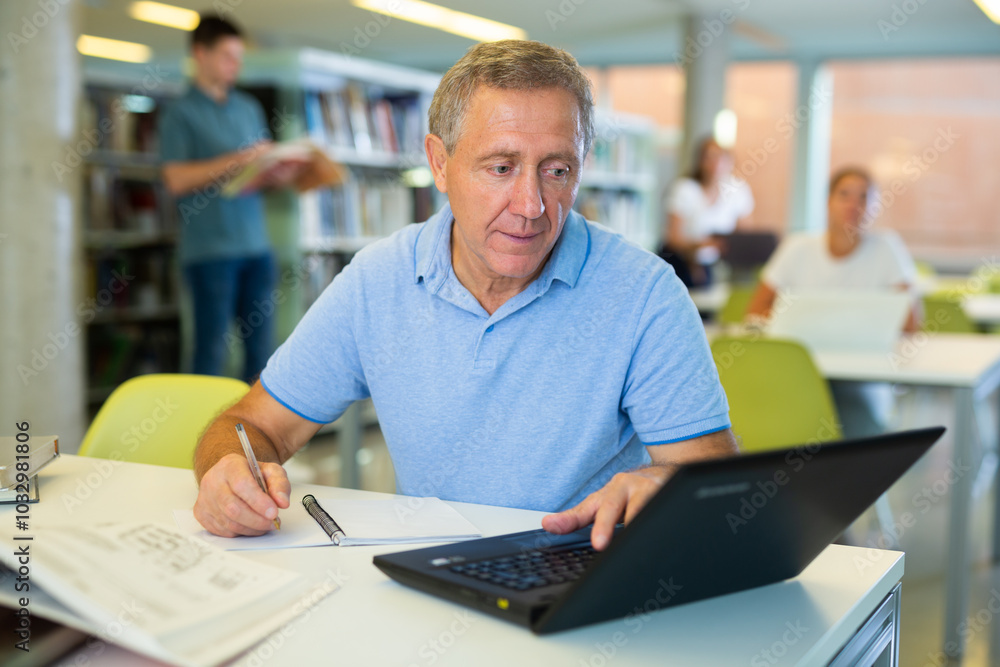 Poster serious man in casual clothes working remotely using a computer and writing in planner n a quiet lib