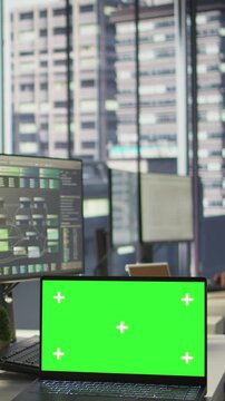 Vertical video Green screen laptop on desk in workspace with admins in background doing software quality assurance. Chroma key notebook in office with woman at work inspecting coding on device, camera
