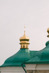 Close-up of golden domes with green roofs, part of a historic religious building, against a pale sky.
