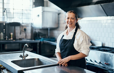 Obraz premium Baker, portrait and happy in cafe kitchen for culinary service, catering and recipe development with apron. Woman, face and smile in bakery for small business, cooking and baking with chef industry