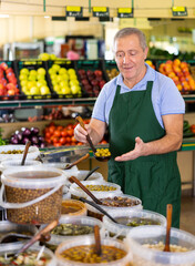 in vegetable department, friendly man - owner of store puts large olives into container for buyer
