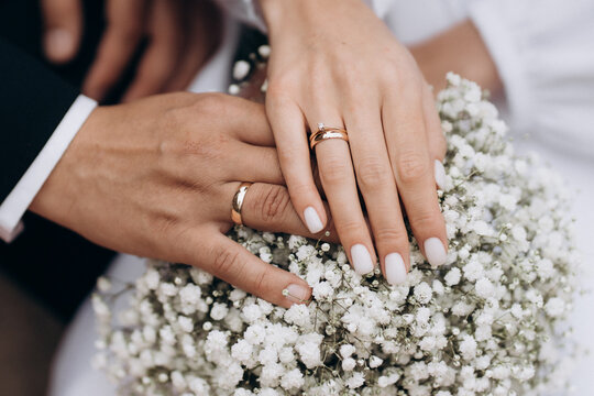 Newly wed couple's hands with wedding rings on a bouquet.