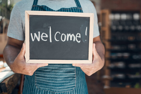 Waiter, hands and sign with welcome at cafe for hospitality, customer service and ready to start day. Barista, person and chalkboard with message at coffee shop entrance for opening at small business