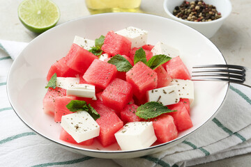 Delicious watermelon salad with mint and feta cheese in bowl served on table, closeup