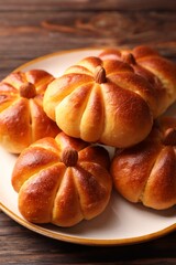 Tasty pumpkin shaped buns on wooden table, closeup