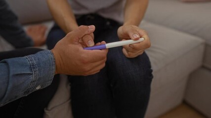 Couple in jeans sitting on a couch together in a living room holding a pregnancy test