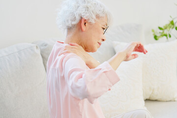 肩凝りのシニア女性の後ろ姿　リビングルーム