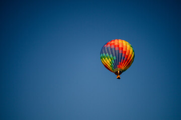 Colorful hot air balloon with red, green, yellow, purple, orange flying in blue sky with flame burning