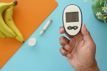 A hand is holding a glucometer alongside bananas and various essential diabetes supplies