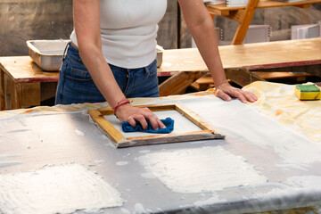 Unrecognizable woman artist creating recycled paper sheets in a bright studio, showcasing the beauty of sustainability through hands-on craftsmanship in the afternoon light