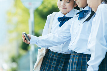 バス停でスマホをみる女子学生